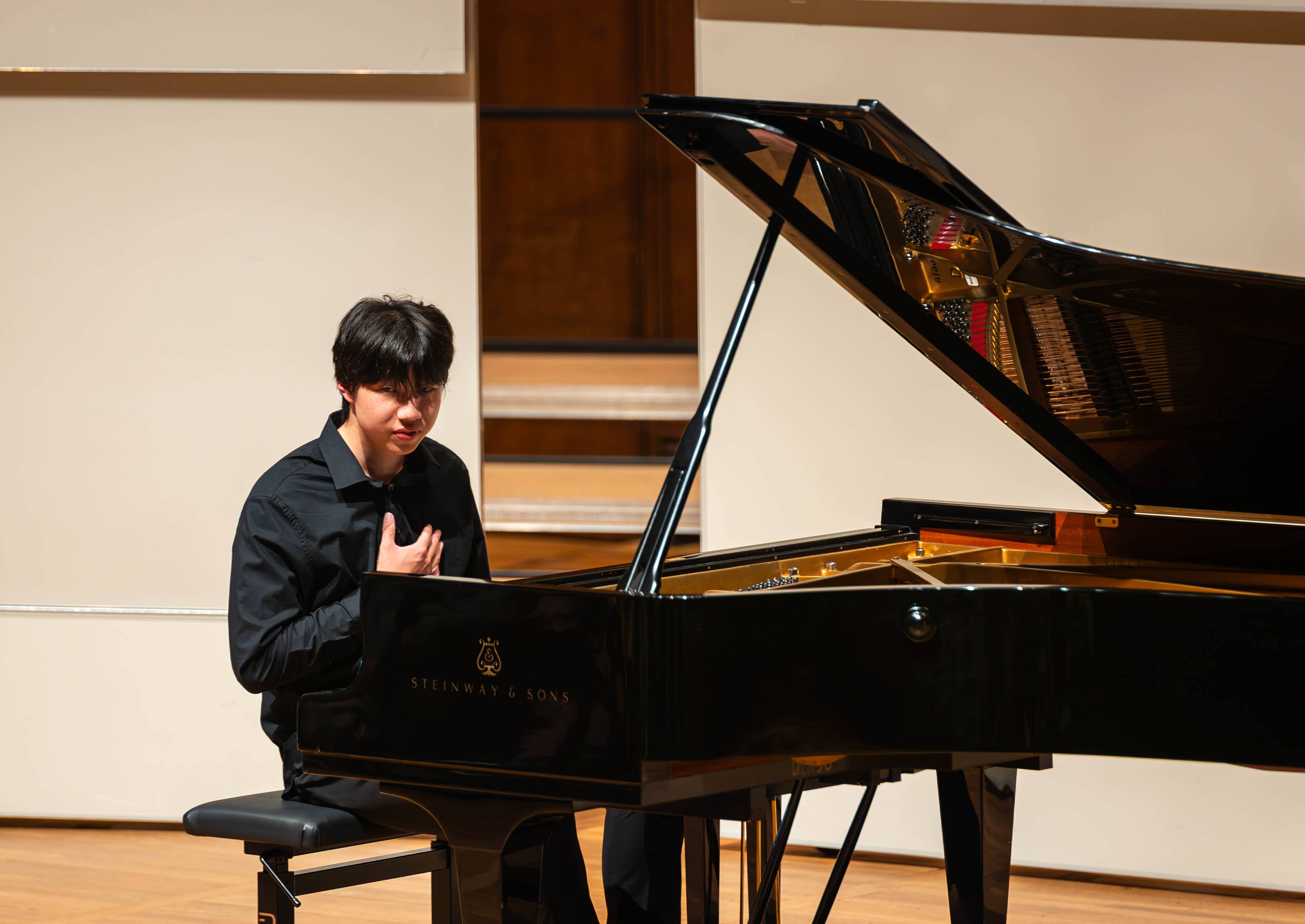 Zhifan Yin seated at the grand piano with a hand at his chest