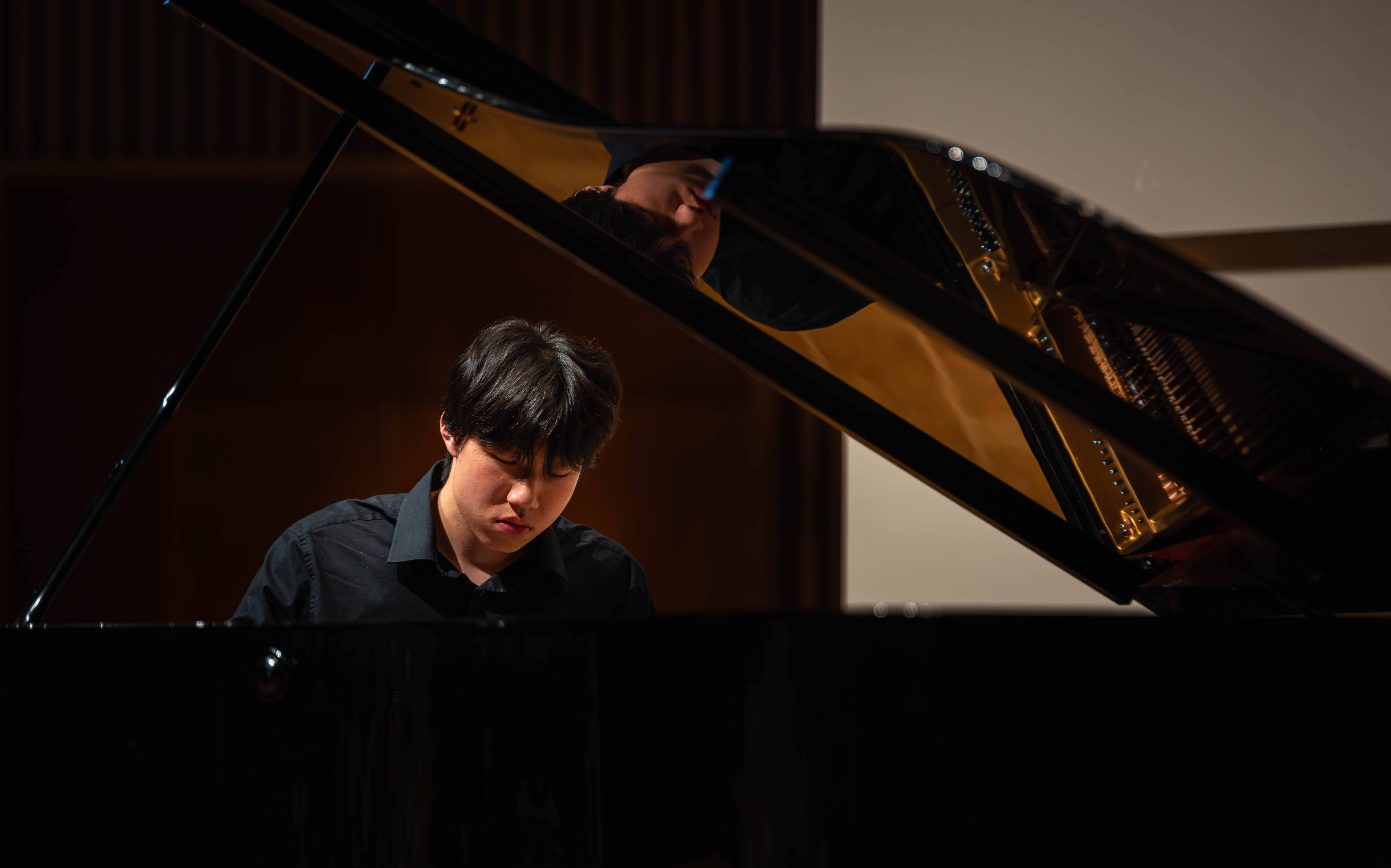 Close-up of Zhifan Yin at the piano, reflected in the raised lid